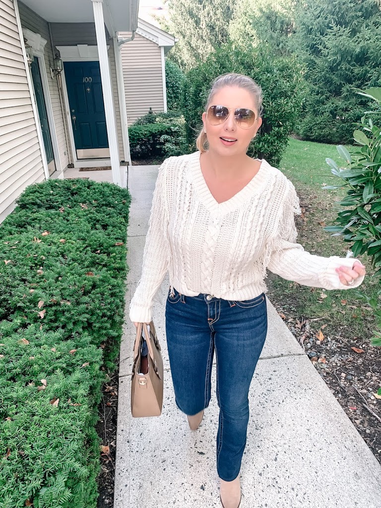 Fall outfit wearing a fringe sweater, bootcut jeans, booties, Ray-Ban sunglasses and a Kate Spade satchel 