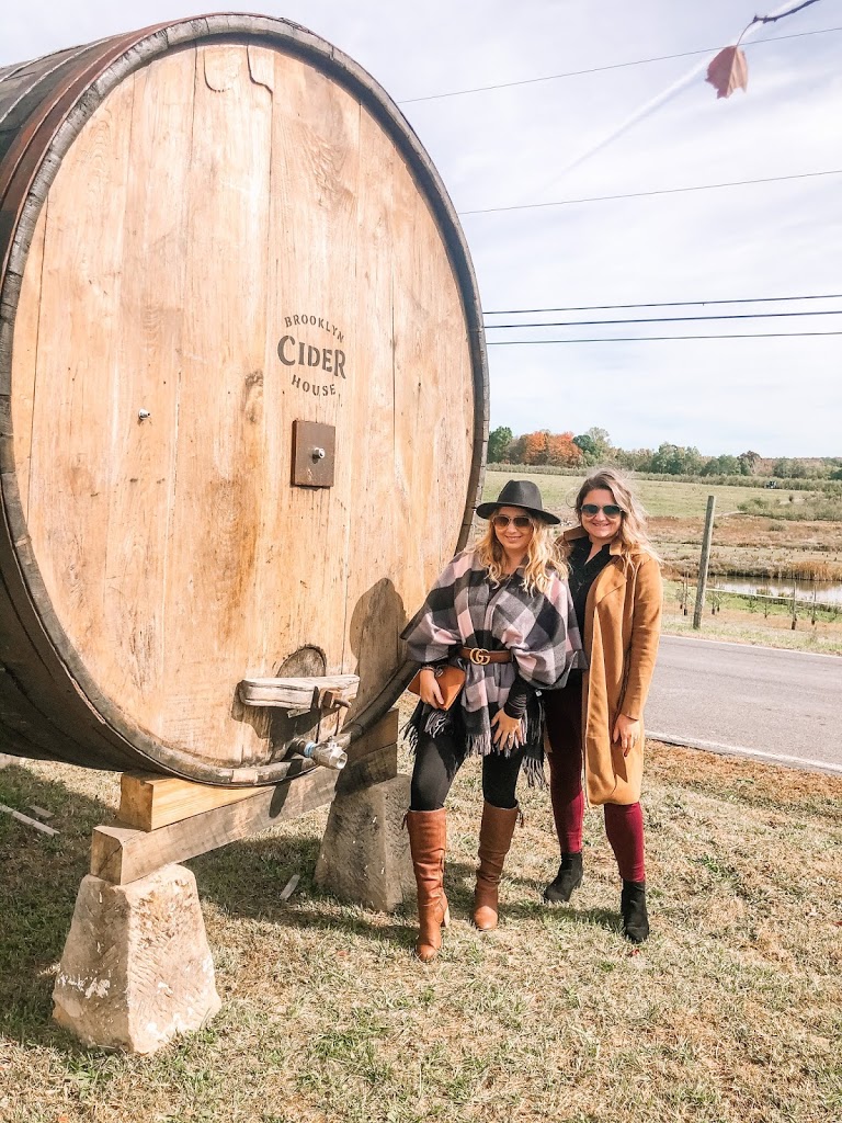 Friends standing in front of a barrel wearing fall style outfits