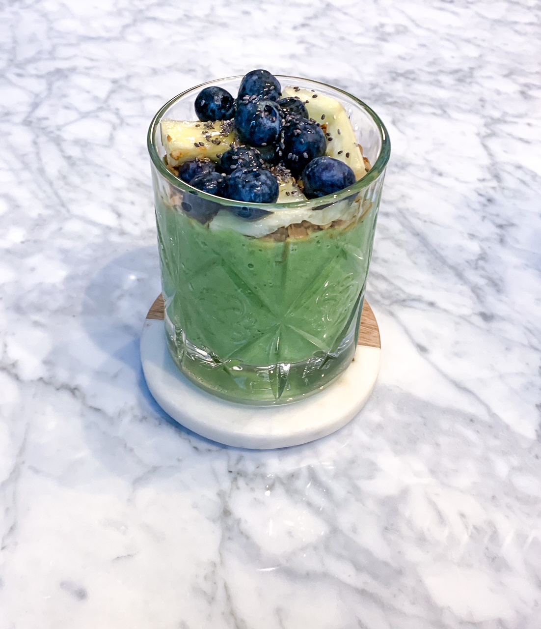 spinach, pineapple and banana smoothie topped with granola, blueberries, pineapples, and chia seeds